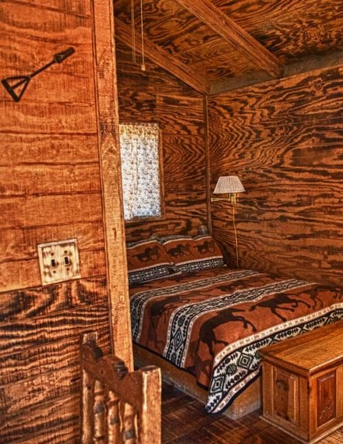 Corner of a large pine cabin with a bed, blanket chest and framed ranch photographs