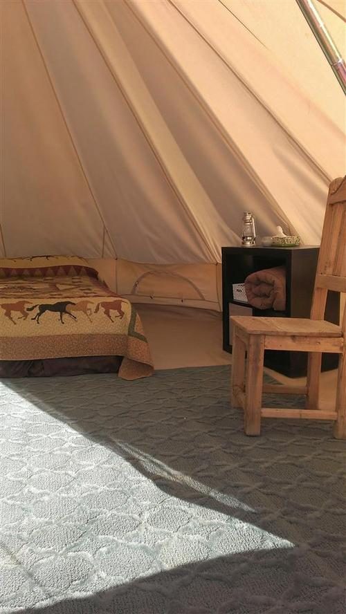 Inside a canvas glamping tent with a made bed, rug and a wooden side table