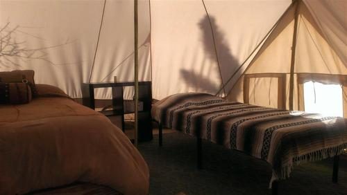Large glamping tent interior with a double bed and a row of twin beds under canvas
