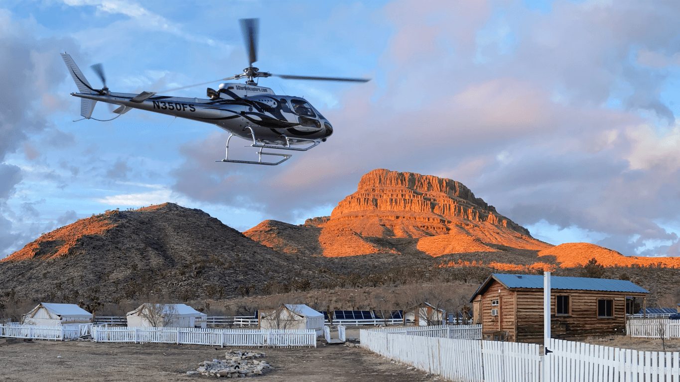 A helicopter lifting off from the ranch with the red mesa lit behind it