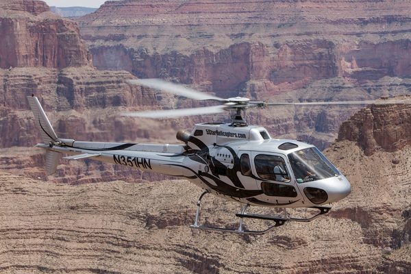 Helicopter flying below the rim of the Grand Canyon above red rock walls