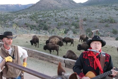 A wrangler on horseback and a musician with a guitar beside the ranch's bison herd